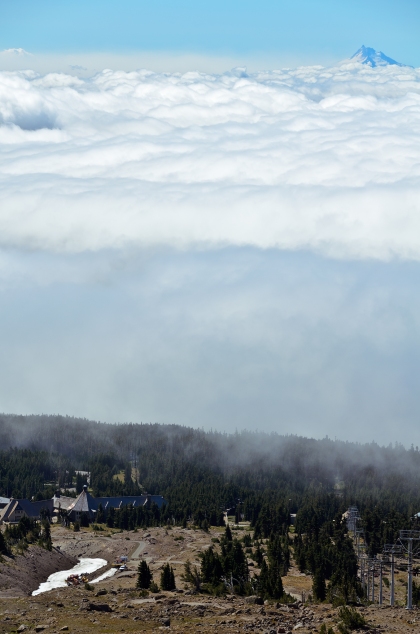 This photo captures Timberline Lodge beneath a blanket of clouds with Mount Jefferson peeking through the top of the cloud cover.
